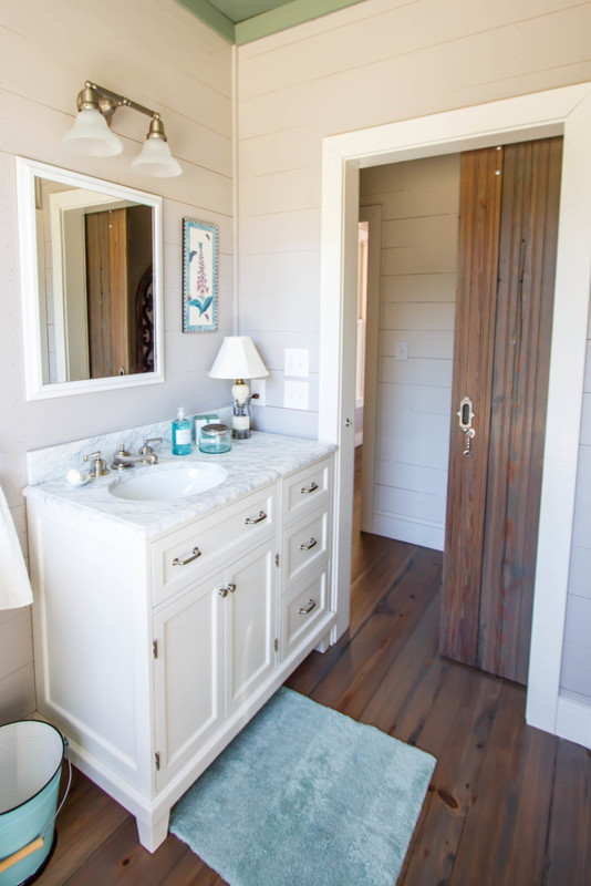 Exempel på ett mellanstort lantligt badrum med dusch, med luckor med infälld panel, vita skåp, ett badkar med tassar, en toalettstol med separat cisternkåpa, vita väggar, mörkt trägolv, ett undermonterad handfat, marmorbänkskiva och brunt golv