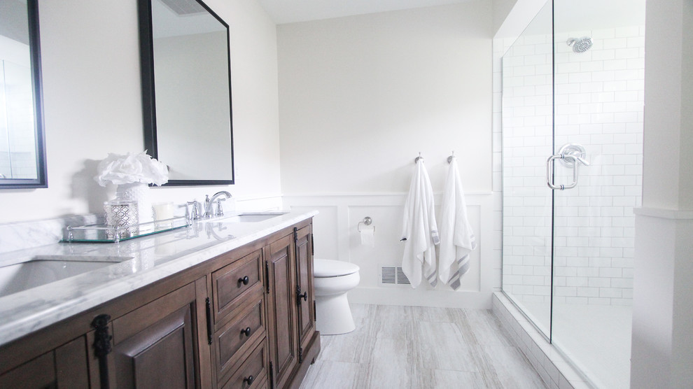Design ideas for a medium sized farmhouse ensuite bathroom in Minneapolis with brown cabinets, a double shower, a two-piece toilet, white tiles, metro tiles, white walls, vinyl flooring, a submerged sink, marble worktops, grey floors, a hinged door and white worktops.