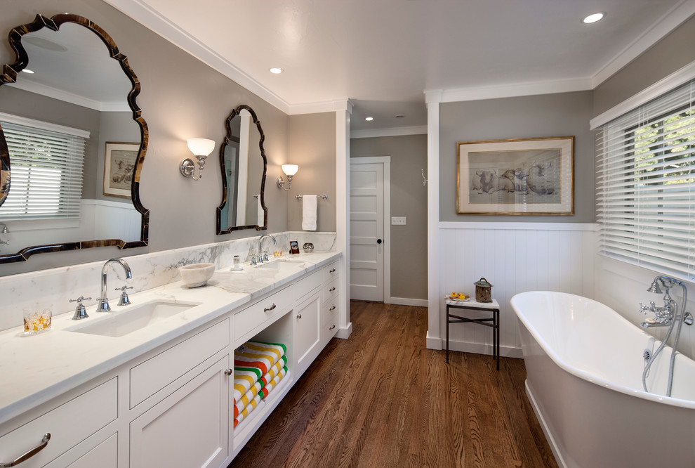 Ejemplo de cuarto de baño clásico con lavabo bajoencimera, armarios estilo shaker, puertas de armario blancas, bañera exenta, paredes grises y suelo de madera oscura