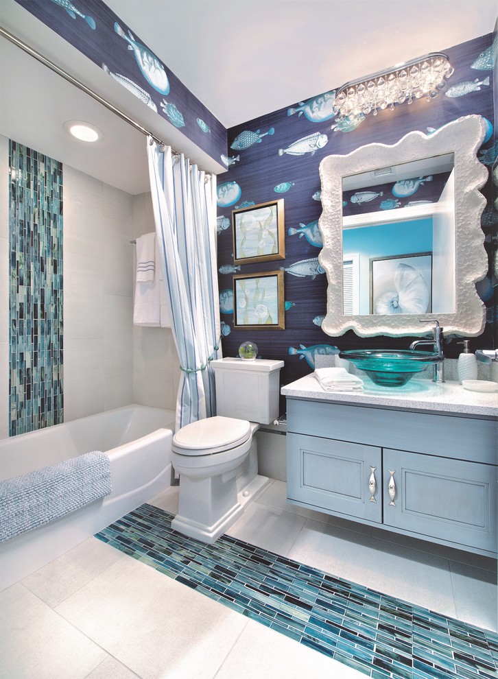 マイアミにある広いビーチスタイルのおしゃれな子供用バスルーム (青いキャビネット、ドロップイン型浴槽、シャワー付き浴槽	、一体型トイレ	、マルチカラーのタイル、モザイクタイル、青い壁、磁器タイルの床、ペデスタルシンク、珪岩の洗面台) の写真