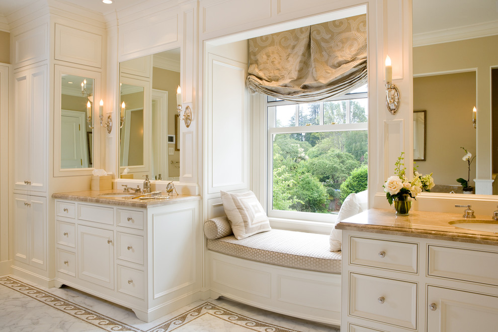 Пример оригинального дизайна: большая главная ванная комната в классическом стиле с белыми фасадами, фасадами с утопленной филенкой, белыми стенами, мраморным полом, врезной раковиной, столешницей из известняка, белым полом и окном