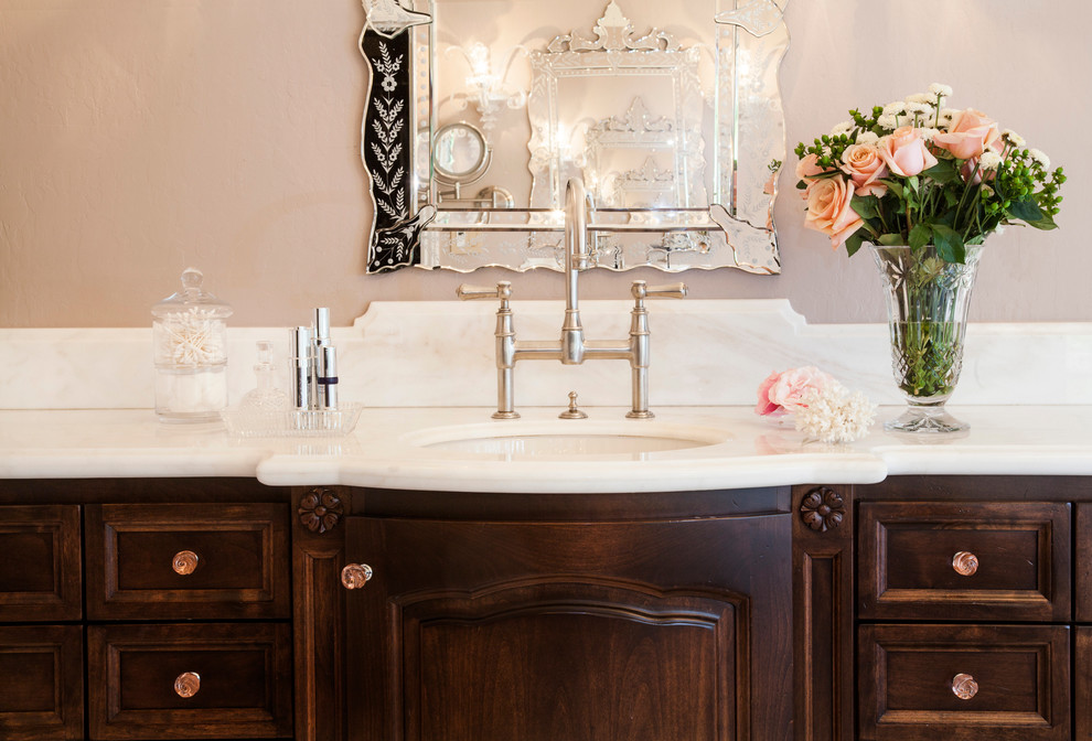 Cette image montre une grande salle de bain principale traditionnelle en bois foncé avec un placard à porte affleurante, une baignoire indépendante, une douche ouverte, WC à poser, un carrelage blanc, un carrelage de pierre, un mur rose, un sol en travertin, un lavabo encastré, un plan de toilette en marbre et un sol beige.
