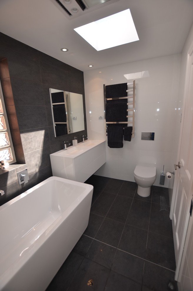 Contemporary bathroom in Sydney with a wall-mounted sink, a freestanding bath, a walk-in shower, flat-panel cabinets, white cabinets, engineered stone worktops, black tiles and porcelain tiles.