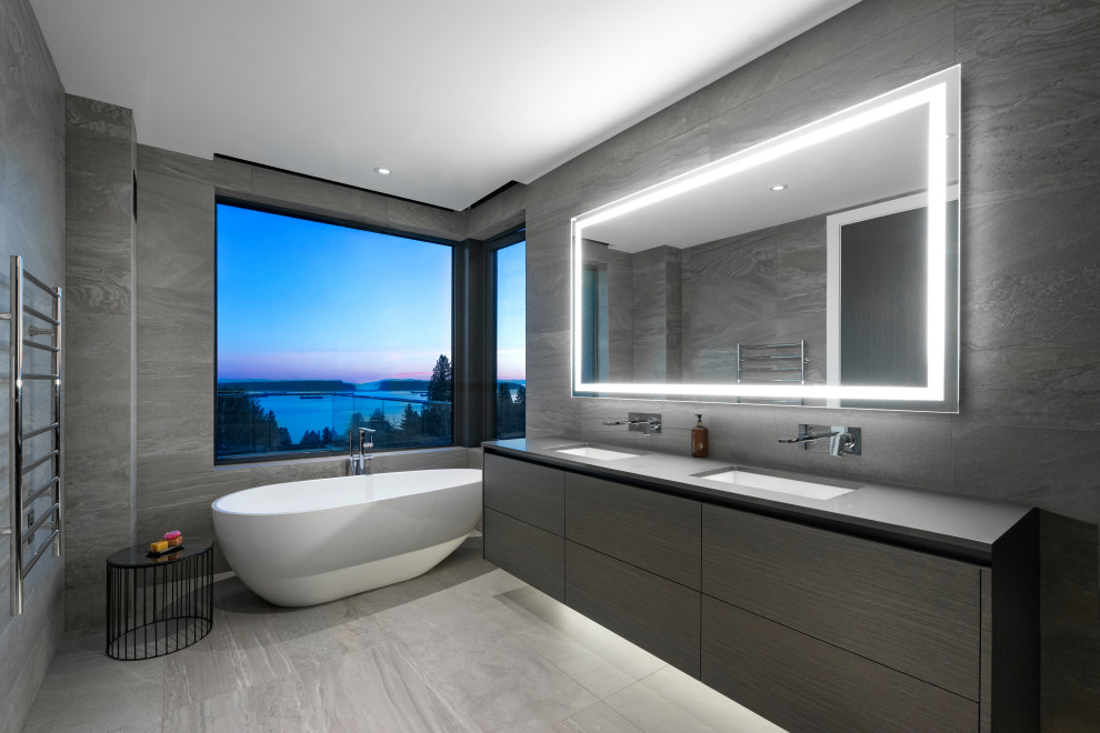 Aménagement d'une salle de bain contemporaine avec un placard à porte plane, des portes de placard grises, une baignoire indépendante, un carrelage gris, un lavabo encastré, un sol gris et un plan de toilette gris.