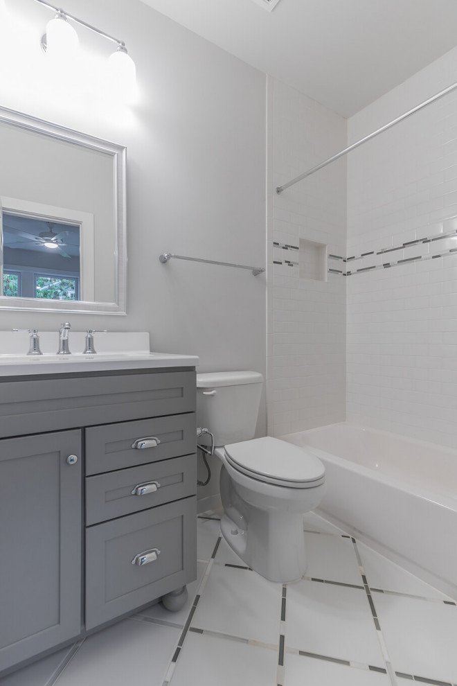 Пример оригинального дизайна: ванная комната среднего размера в стиле неоклассика (современная классика) с фасадами в стиле шейкер, серыми фасадами, ванной в нише, душем над ванной, раздельным унитазом, белой плиткой, плиткой кабанчик, серыми стенами, полом из мозаичной плитки, монолитной раковиной, столешницей из искусственного камня, белым полом, шторкой для ванной, белой столешницей, нишей, тумбой под одну раковину и встроенной тумбой