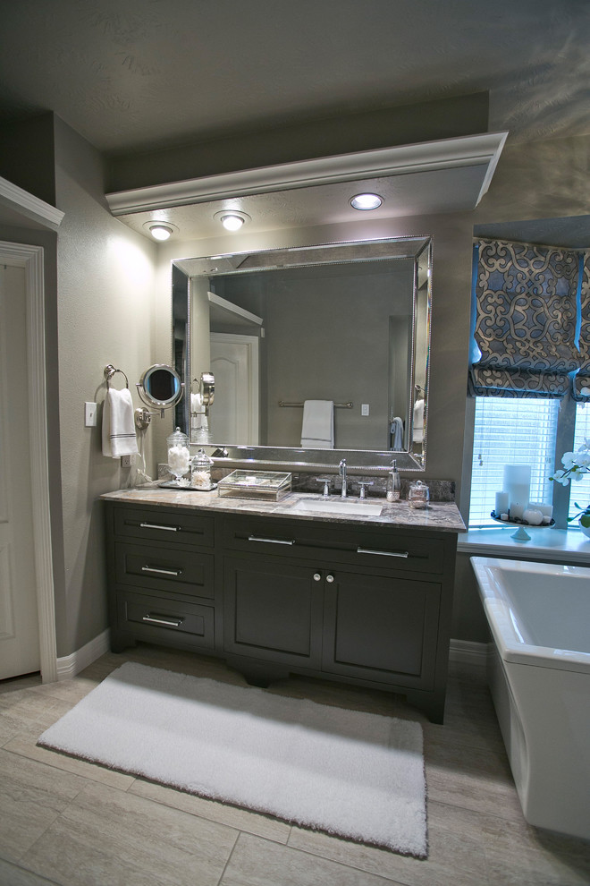 Inredning av ett klassiskt badrum, med ett undermonterad handfat, möbel-liknande, svarta skåp, marmorbänkskiva, ett fristående badkar, en kantlös dusch, en toalettstol med hel cisternkåpa, grå kakel och keramikplattor