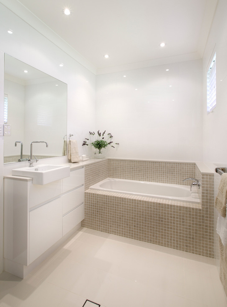 Cette photo montre une salle de bain moderne avec un placard à porte plane, des portes de placard blanches, une baignoire posée, un carrelage beige, mosaïque et un mur blanc.