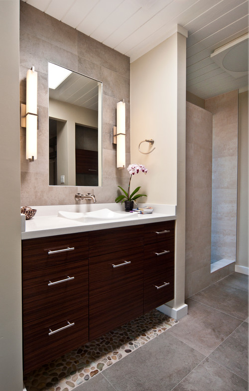Modern bathroom cabinets in dark wood with flat-panel drawers, white quartz vanity and integrated sink, mirror with sconces, and walk-in shower.