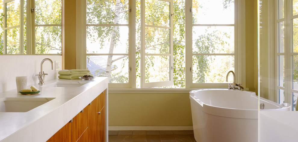 Cette photo montre une petite salle de bain principale moderne en bois brun avec une baignoire indépendante, un placard à porte plane, WC à poser, un carrelage marron, des dalles de pierre, un mur vert, un lavabo encastré et un plan de toilette en calcaire.