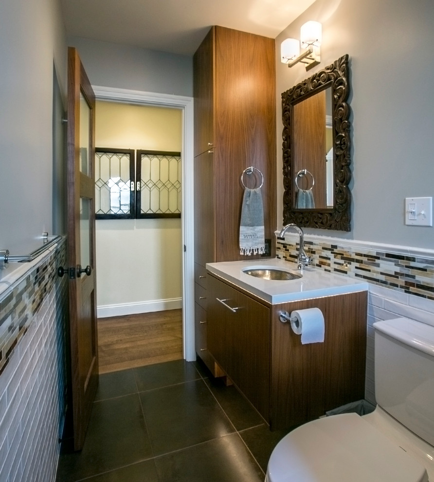 Klassisk inredning av ett litet badrum med dusch, med ett nedsänkt handfat, släta luckor, skåp i mellenmörkt trä, bänkskiva i kvarts, en dusch i en alkov, en toalettstol med separat cisternkåpa, flerfärgad kakel, glaskakel, grå väggar och klinkergolv i keramik