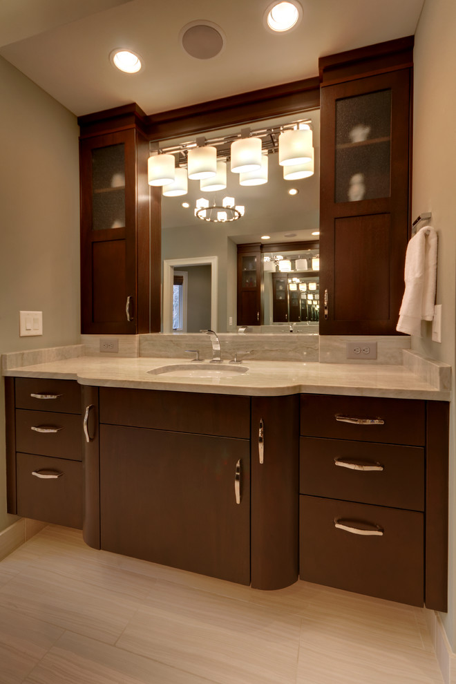 Cette image montre une salle de bain design en bois foncé avec un placard à porte plane, une baignoire indépendante, WC à poser, un carrelage gris, un lavabo encastré, un plan de toilette en quartz et un mur gris.