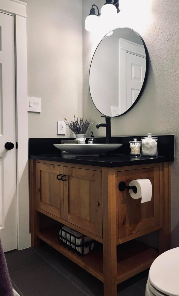 Photo of a small country shower room bathroom in Austin with freestanding cabinets, medium wood cabinets, a one-piece toilet, white walls, ceramic flooring, a vessel sink, granite worktops, grey floors and black worktops.