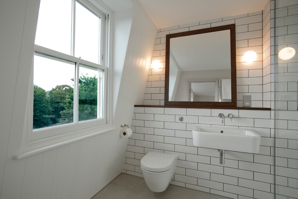 Foto på ett funkis badrum, med en vägghängd toalettstol, vit kakel, klinkergolv i keramik, ett väggmonterat handfat och träbänkskiva