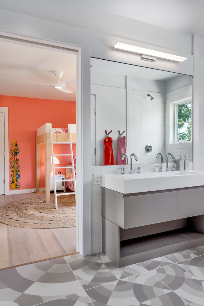 Bild på ett stort minimalistiskt vit vitt badrum för barn, med släta luckor, grå skåp, en hörndusch, vit kakel, porslinskakel, vita väggar, klinkergolv i porslin, ett avlångt handfat, bänkskiva i akrylsten och flerfärgat golv