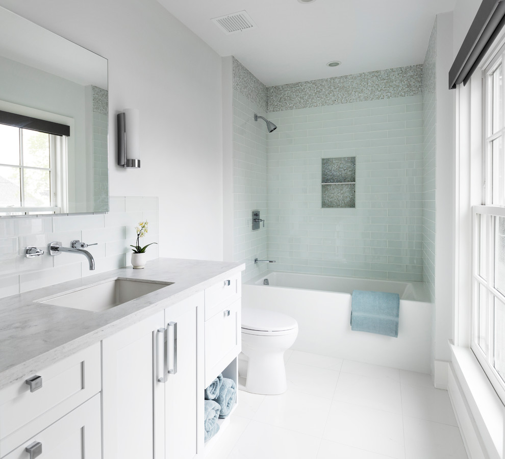 Bild på ett mellanstort maritimt en-suite badrum, med skåp i shakerstil, vita skåp, ett badkar i en alkov, en dusch/badkar-kombination, en toalettstol med separat cisternkåpa, blå kakel, glaskakel, vita väggar, klinkergolv i porslin, ett undermonterad handfat, marmorbänkskiva, vitt golv och med dusch som är öppen