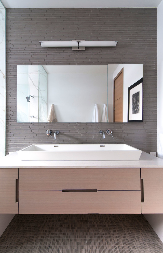 Diseño de cuarto de baño rectangular minimalista con lavabo de seno grande, armarios con paneles lisos, puertas de armario de madera clara, baldosas y/o azulejos grises y baldosas y/o azulejos de vidrio