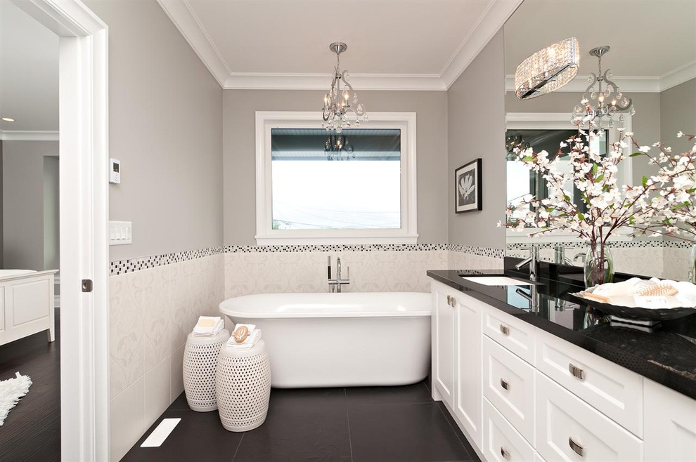 他の地域にあるコンテンポラリースタイルのおしゃれな浴室 (アンダーカウンター洗面器、落し込みパネル扉のキャビネット、白いキャビネット、置き型浴槽、白いタイル、黒い床、黒い洗面カウンター) の写真