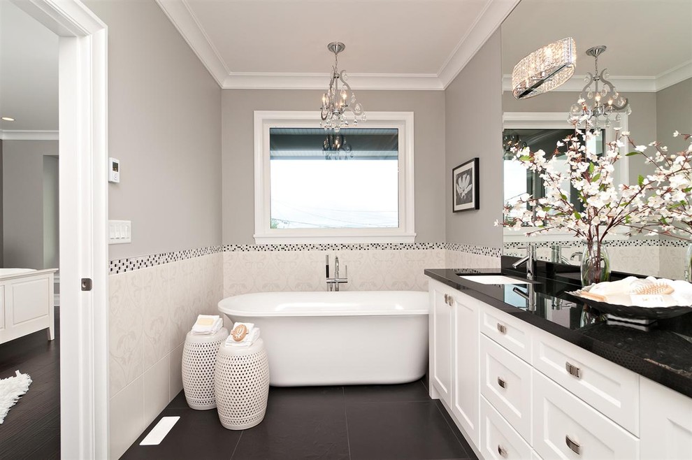 Trendy white tile black floor freestanding bathtub photo in Other with an undermount sink, recessed-panel cabinets, white cabinets and black countertops