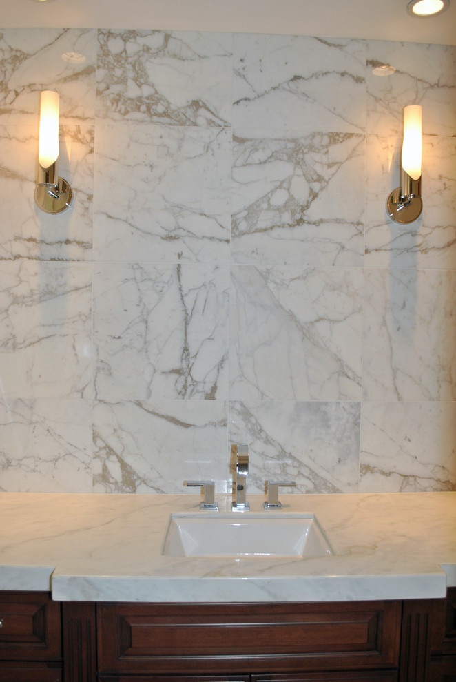 Inredning av ett klassiskt badrum, med ett undermonterad handfat, luckor med upphöjd panel, skåp i mellenmörkt trä, marmorbänkskiva, vit kakel och stenkakel