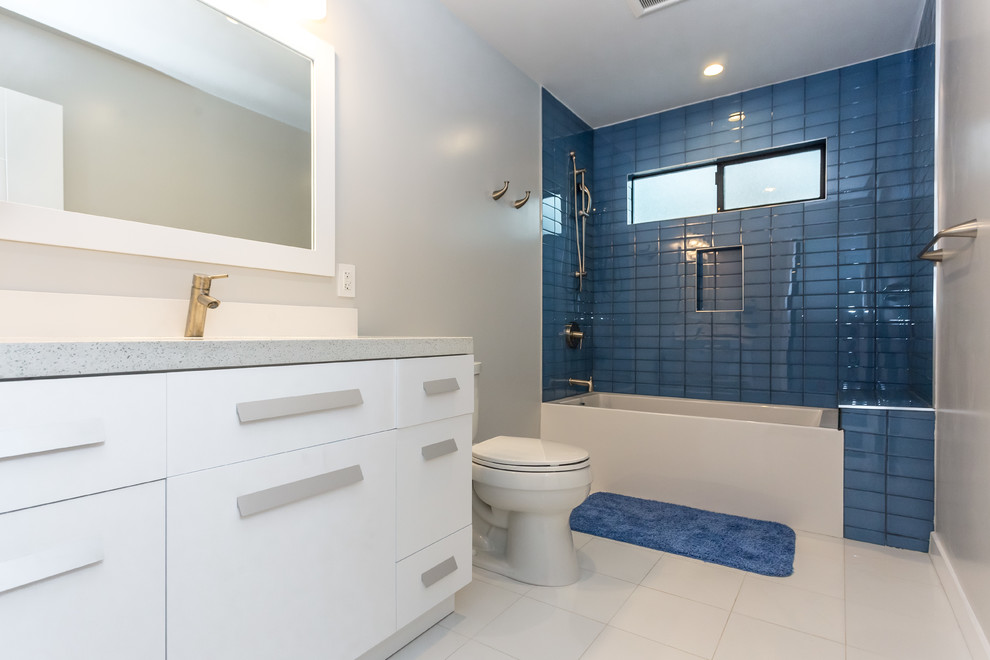 Стильный дизайн: большая ванная комната в современном стиле с плоскими фасадами, белыми фасадами, ванной в нише, раздельным унитазом, синей плиткой, стеклянной плиткой, серыми стенами, полом из керамогранита, врезной раковиной, столешницей из искусственного кварца, душем над ванной и душевой кабиной - последний тренд
