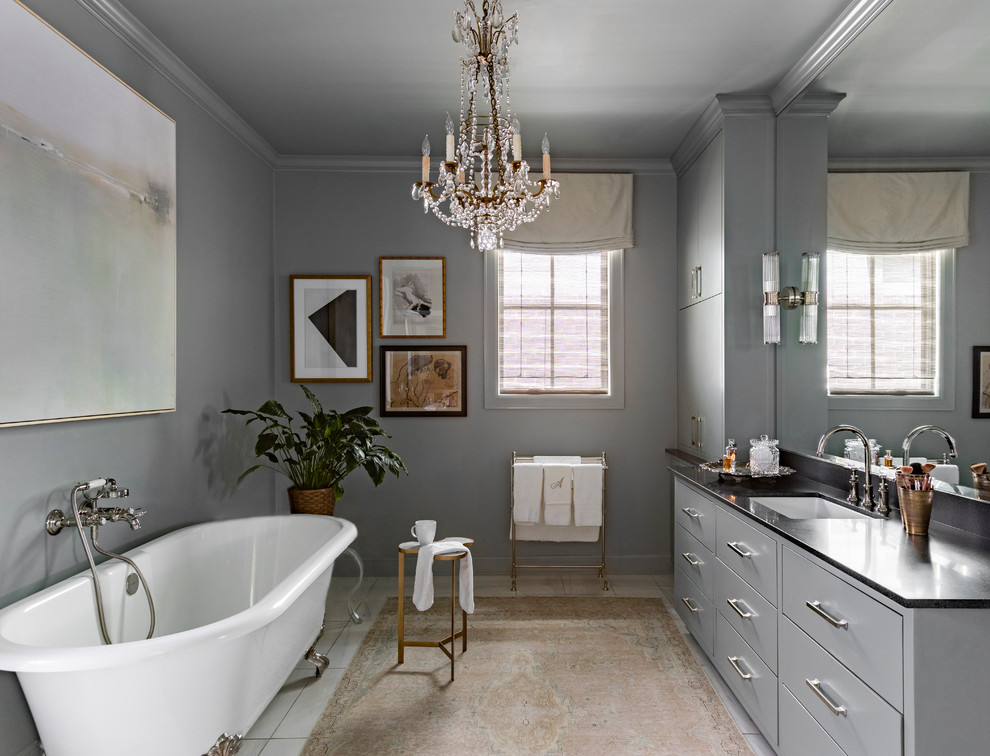 Inredning av ett klassiskt svart svart badrum, med släta luckor, grå skåp, ett badkar med tassar, grå väggar, ett undermonterad handfat och vitt golv