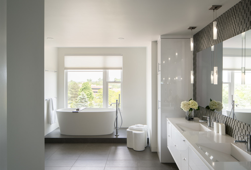 This is an example of a medium sized modern ensuite bathroom in Denver with flat-panel cabinets, white cabinets, a freestanding bath, white walls, grey tiles, mosaic tiles, porcelain flooring, a trough sink, solid surface worktops and grey floors.