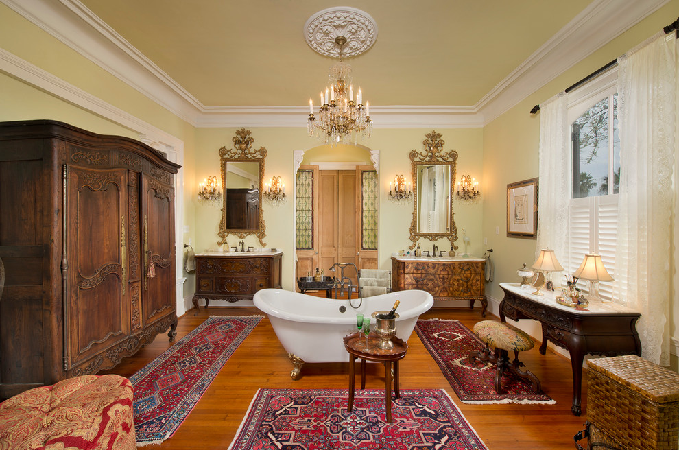 Inredning av ett klassiskt en-suite badrum, med skåp i mellenmörkt trä, ett fristående badkar, gula väggar, mellanmörkt trägolv och luckor med infälld panel