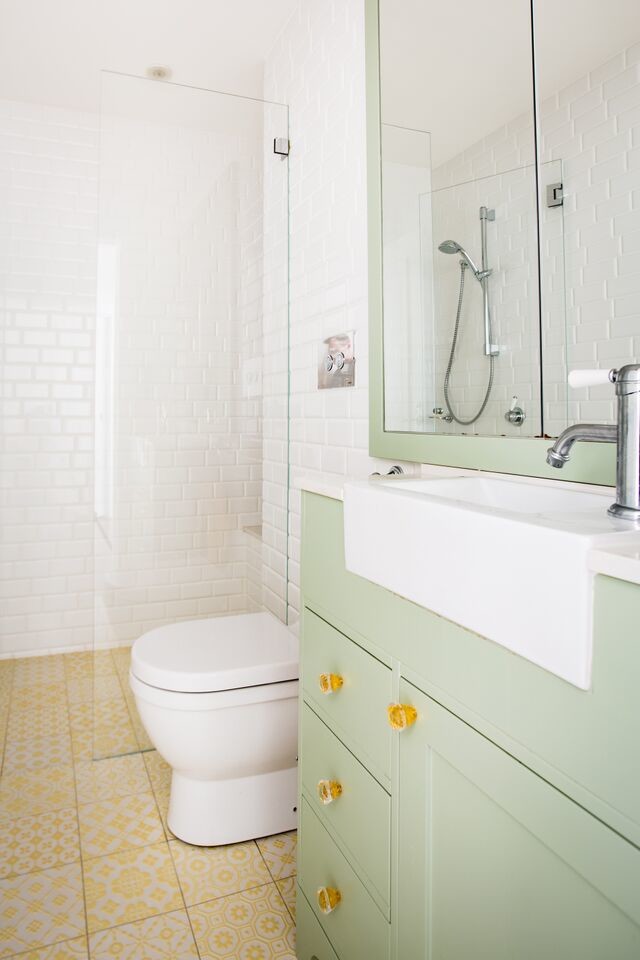 Стильный дизайн: ванная комната среднего размера в стиле модернизм с зелеными фасадами, инсталляцией, керамической плиткой, белыми стенами, полом из керамической плитки, столешницей из искусственного кварца, душевой кабиной, фасадами в стиле шейкер, душем в нише, белой плиткой, накладной раковиной, желтым полом и душем с распашными дверями - последний тренд