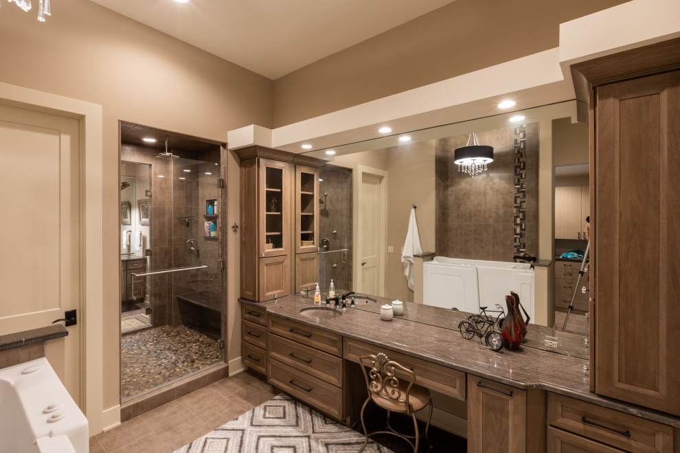 Photo of an expansive rustic ensuite bathroom in Omaha with recessed-panel cabinets, dark wood cabinets, a double shower, brown tiles, beige walls, a submerged sink, granite worktops, brown floors, a hinged door and brown worktops.