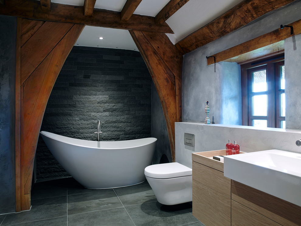Cette image montre une salle de bain rustique de taille moyenne avec un plan vasque, une baignoire indépendante, une douche à l'italienne, WC suspendus, un carrelage gris, un carrelage de pierre, un mur gris et un sol en carrelage de porcelaine.