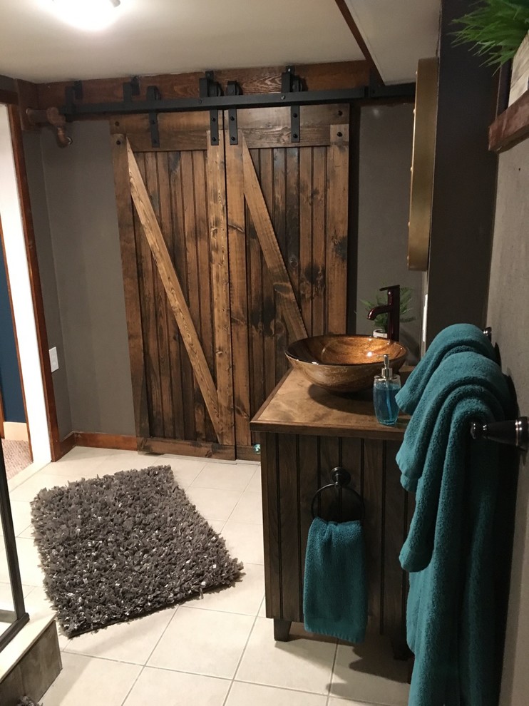Inspiration for a small rustic multicolored tile and ceramic tile ceramic tile and beige floor corner shower remodel in Boston with beaded inset cabinets, distressed cabinets, a two-piece toilet, gray walls, a vessel sink, wood countertops and a hinged shower door