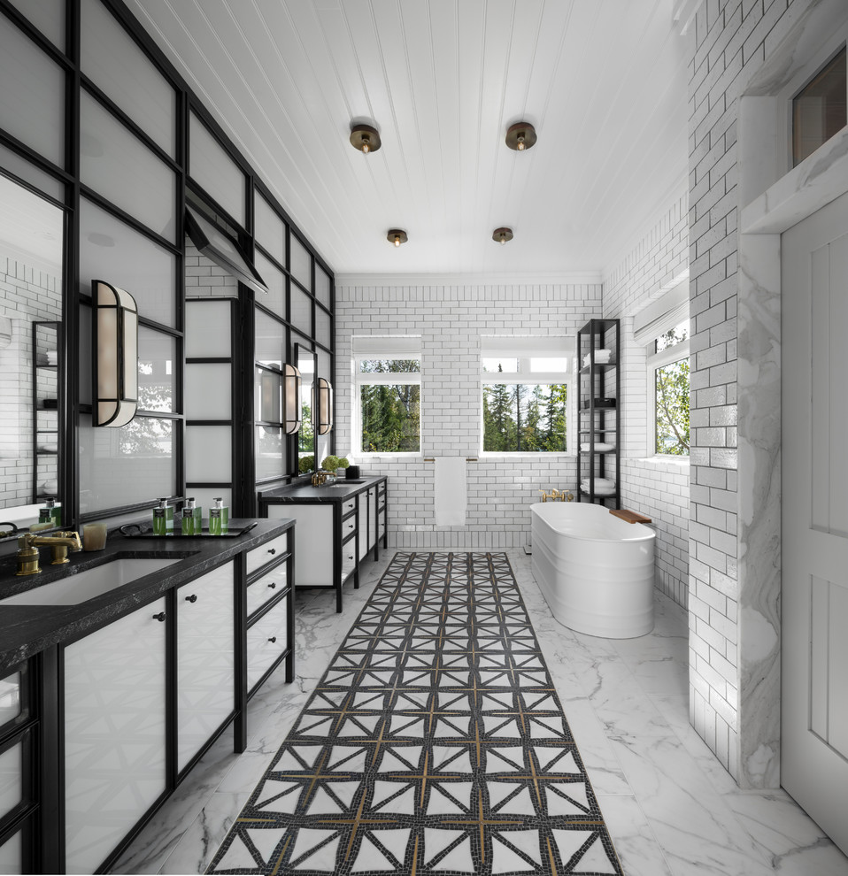 На фото: главная ванная комната в стиле неоклассика (современная классика) с отдельно стоящей ванной, белой плиткой, плиткой кабанчик, белыми стенами, врезной раковиной, разноцветным полом, черной столешницей, зеркалом с подсветкой и плоскими фасадами
