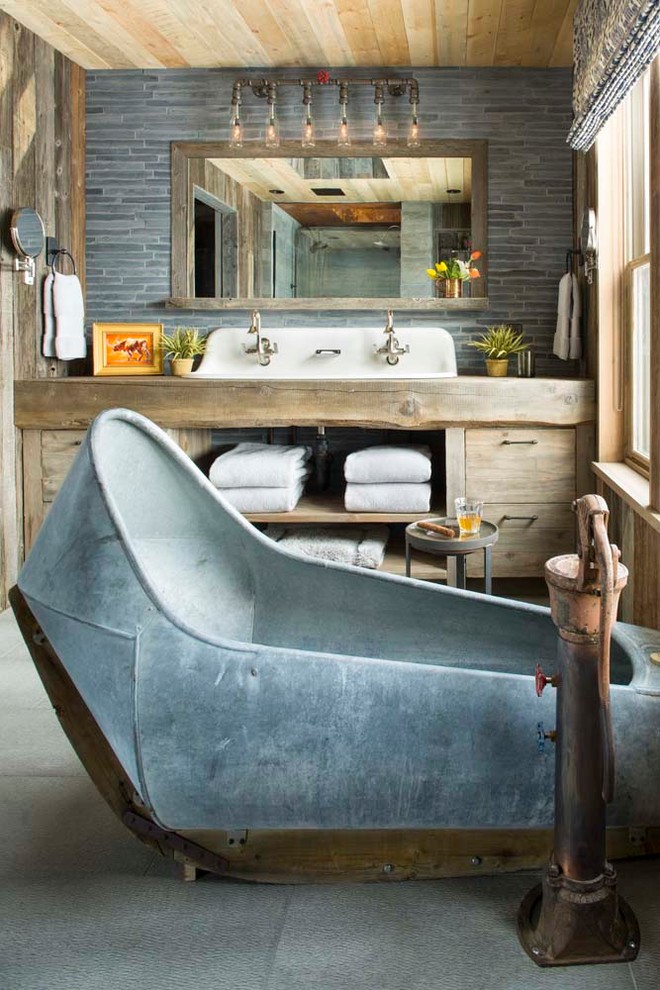 На фото: ванная комната в стиле рустика с плоскими фасадами, светлыми деревянными фасадами, столешницей из дерева, отдельно стоящей ванной, серой плиткой и коричневой столешницей с