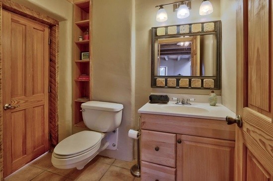 アルバカーキにある中くらいなラスティックスタイルのおしゃれな浴室 (レイズドパネル扉のキャビネット、淡色木目調キャビネット、壁掛け式トイレ、ベージュの壁、セラミックタイルの床、一体型シンク、茶色い床) の写真