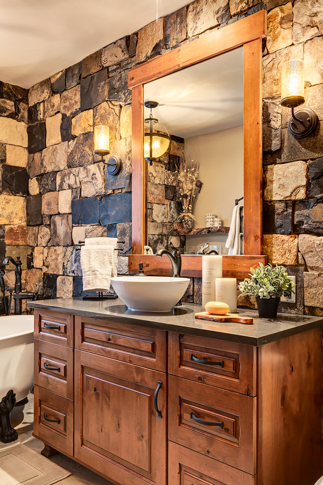 Inspiration for a small rustic ensuite bathroom in Calgary with freestanding cabinets, medium wood cabinets, a claw-foot bath, a one-piece toilet, multi-coloured tiles, stone slabs, beige walls, ceramic flooring, a pedestal sink and engineered stone worktops.