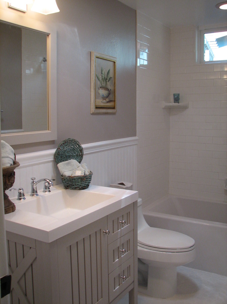 Exemple d'une salle de bain tendance de taille moyenne avec un lavabo intégré, un placard à porte shaker, des portes de placard grises, un plan de toilette en surface solide, une baignoire en alcôve, un combiné douche/baignoire, WC à poser, un carrelage blanc, des carreaux de céramique, un mur gris et un sol en carrelage de céramique.