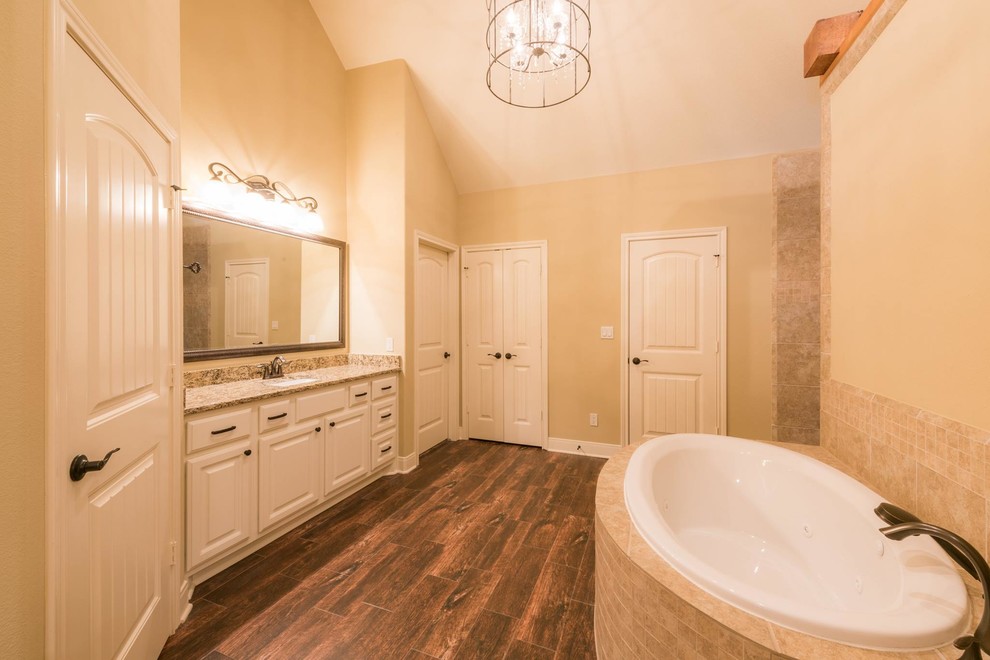 Inredning av ett amerikanskt mellanstort en-suite badrum, med luckor med upphöjd panel, vita skåp, ett platsbyggt badkar, beige kakel, stenkakel, beige väggar, mörkt trägolv, ett undermonterad handfat och granitbänkskiva