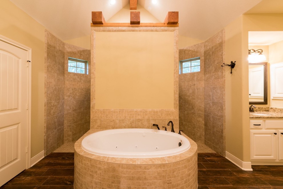 Exemple d'une salle de bain principale craftsman de taille moyenne avec un placard avec porte à panneau surélevé, des portes de placard blanches, une baignoire posée, une douche à l'italienne, un carrelage beige, un carrelage de pierre, un mur beige, parquet foncé, un lavabo encastré et un plan de toilette en granite.