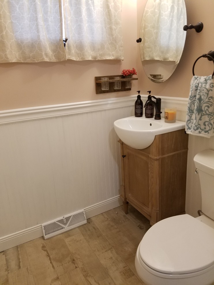 Modelo de cuarto de baño campestre pequeño con armarios estilo shaker, puertas de armario de madera oscura, sanitario de dos piezas, paredes rosas, suelo de madera clara, aseo y ducha y lavabo sobreencimera