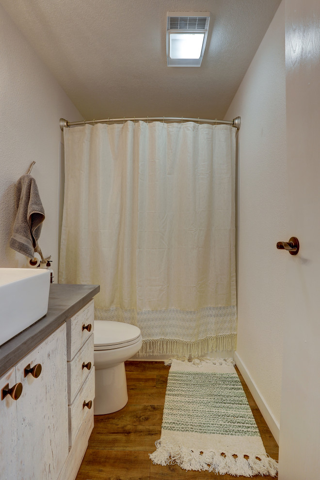 Inspiration pour une petite salle de bain chalet en bois vieilli avec un mur blanc, un sol marron, un plan de toilette gris, un placard à porte plane, une baignoire en alcôve, WC à poser, sol en stratifié, une vasque, un plan de toilette en surface solide et une cabine de douche avec un rideau.