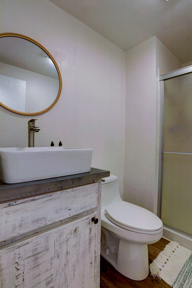 Свежая идея для дизайна: маленькая ванная комната в стиле рустика с искусственно-состаренными фасадами, душевой кабиной, серой столешницей, плоскими фасадами, душем в нише, унитазом-моноблоком, белыми стенами, полом из ламината, настольной раковиной, столешницей из искусственного камня, коричневым полом и душем с раздвижными дверями для на участке и в саду - отличное фото интерьера