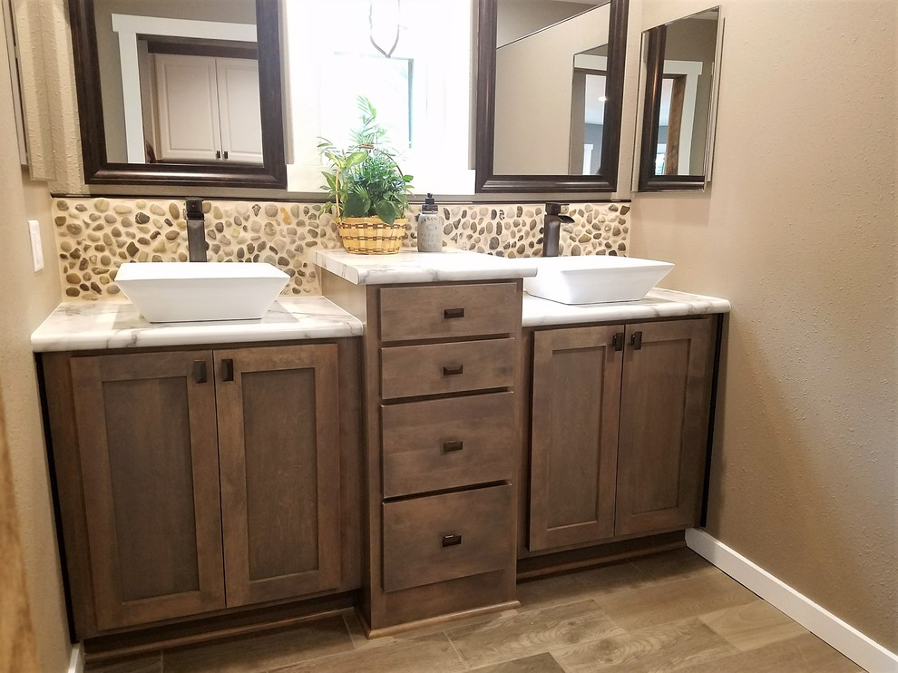 Mid-sized country master pebble tile, beige tile and brown tile medium tone wood floor and brown floor bathroom photo in Other with shaker cabinets, gray cabinets, a vessel sink, laminate countertops, beige walls and beige countertops