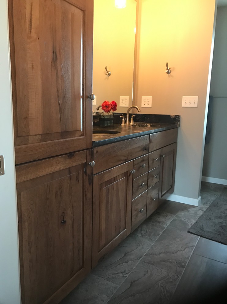 Example of a mid-sized mountain style master ceramic tile and gray floor bathroom design in Other with raised-panel cabinets, medium tone wood cabinets, a one-piece toilet, gray walls, an undermount sink and granite countertops