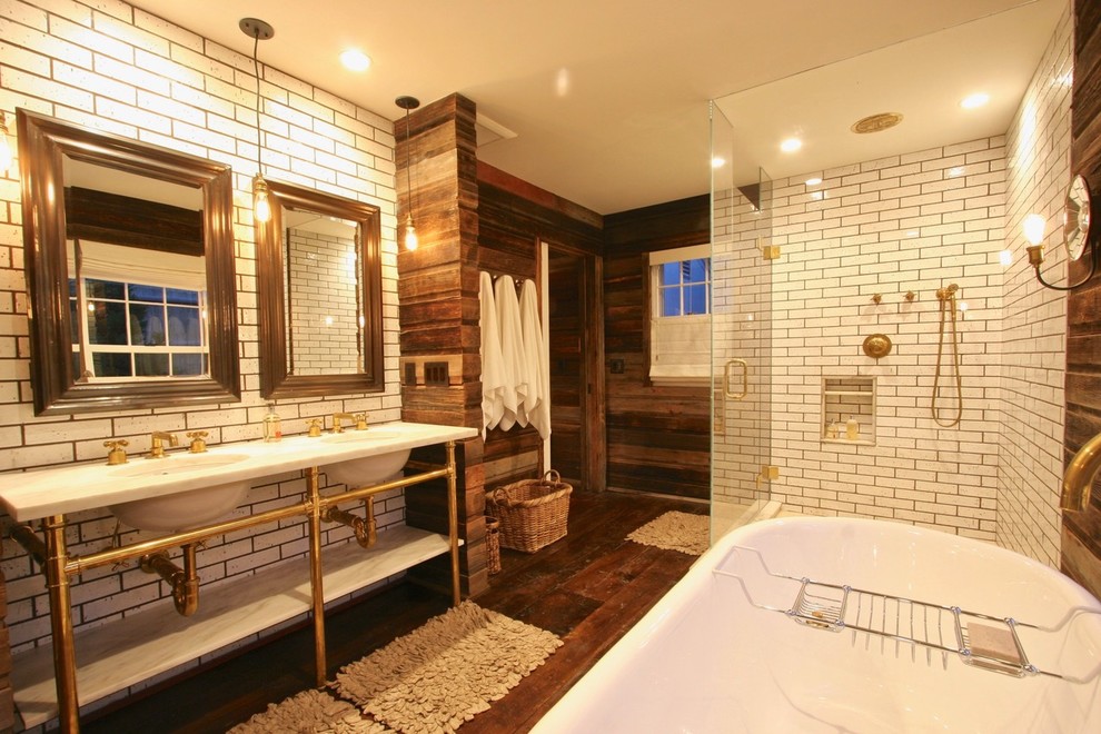 Cette photo montre une grande salle de bain principale montagne avec un placard sans porte, une baignoire indépendante, une douche d'angle, un carrelage blanc, un mur marron, un sol en bois brun, un lavabo encastré, un sol marron et une cabine de douche à porte battante.