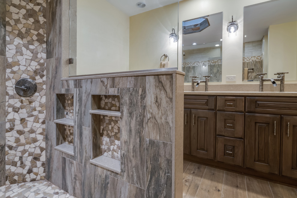 Design ideas for a large rustic ensuite bathroom in Philadelphia with raised-panel cabinets, distressed cabinets, a built-in shower, a two-piece toilet, grey tiles, porcelain tiles, beige walls, porcelain flooring, engineered stone worktops, brown floors, an open shower and beige worktops.