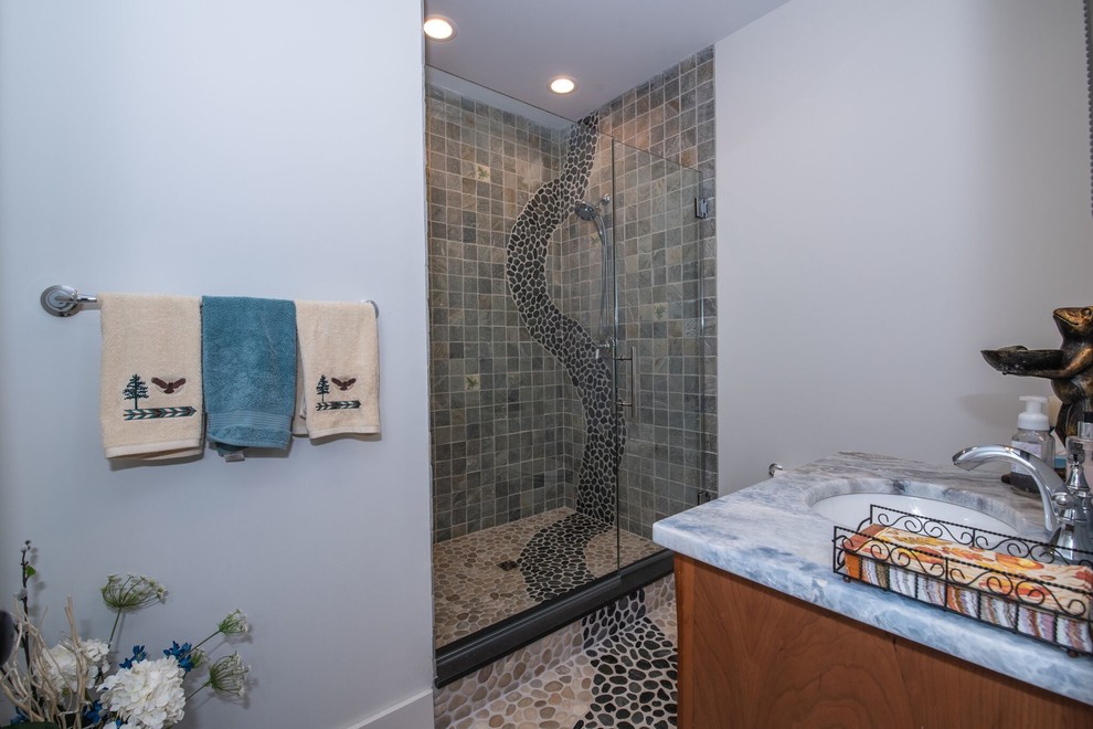 Modern inredning av ett mellanstort grå grått badrum med dusch, med luckor med infälld panel, bruna skåp, en dusch i en alkov, en toalettstol med separat cisternkåpa, flerfärgad kakel, stenkakel, grå väggar, klinkergolv i småsten, ett nedsänkt handfat, marmorbänkskiva, flerfärgat golv och dusch med gångjärnsdörr