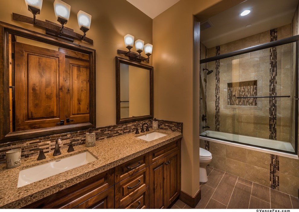This is an example of a medium sized rustic bathroom in Sacramento with raised-panel cabinets, medium wood cabinets, an alcove bath, a two-piece toilet, brown tiles, porcelain tiles, brown walls, porcelain flooring, a submerged sink and engineered stone worktops.