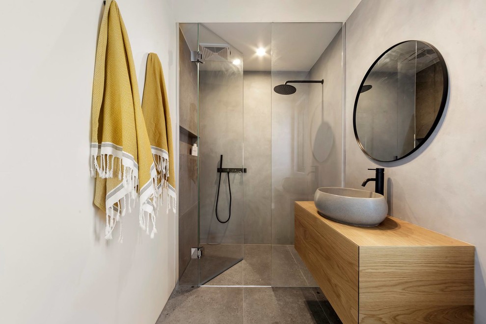 Bild på ett mellanstort funkis badrum, med släta luckor, skåp i ljust trä, en dusch i en alkov, grå kakel, grå väggar, cementgolv, ett fristående handfat, träbänkskiva, grått golv och dusch med gångjärnsdörr