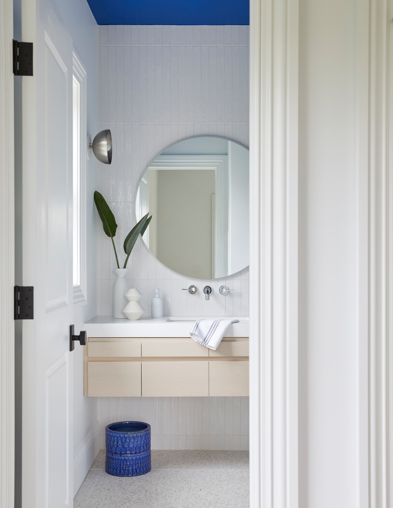 Modernes Badezimmer mit flächenbündigen Schrankfronten, hellen Holzschränken, weißen Fliesen, Unterbauwaschbecken, grauem Boden, weißer Waschtischplatte, Einzelwaschbecken und schwebendem Waschtisch in New York