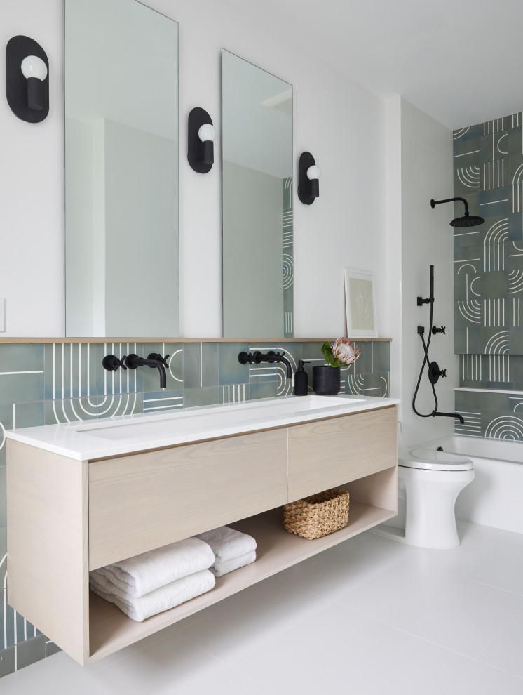 This is an example of a contemporary bathroom in New York with flat-panel cabinets, light wood cabinets, an alcove bath, green tiles, white walls, a trough sink, grey floors, white worktops, double sinks and a floating vanity unit.